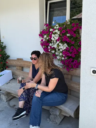 Zwei Frauen sitzen auf der Bank vor der Hauswand mit blühenden Blumenkästen