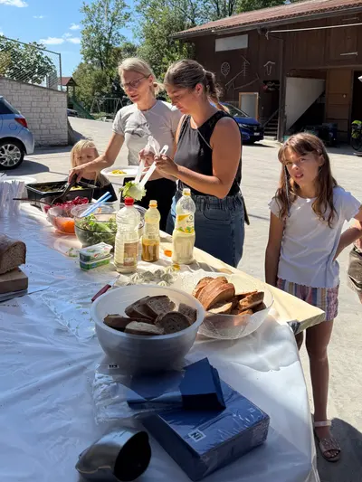 Personen am Buffet, davor Brot und Schüsseln auf dem gedeckten Tisch