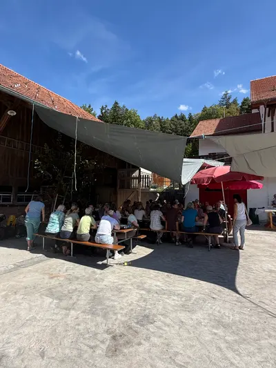 Blick über den Hof der Sennweid: Sonnensegel, Festbänke und Gäste unter blauem Himmel