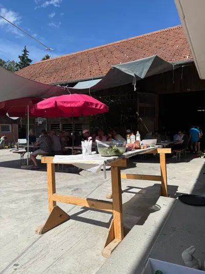 Gedeckter Tisch unter dem roten Schirm, im Hintergrund der Hof